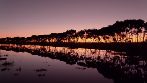 Beautiful-sunset-behind-tree-lined-lake-of-water-with-incredible-sky