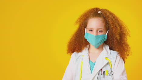 studio portrait of girl dressed as doctor or surgeon wearing face mask against yellow background