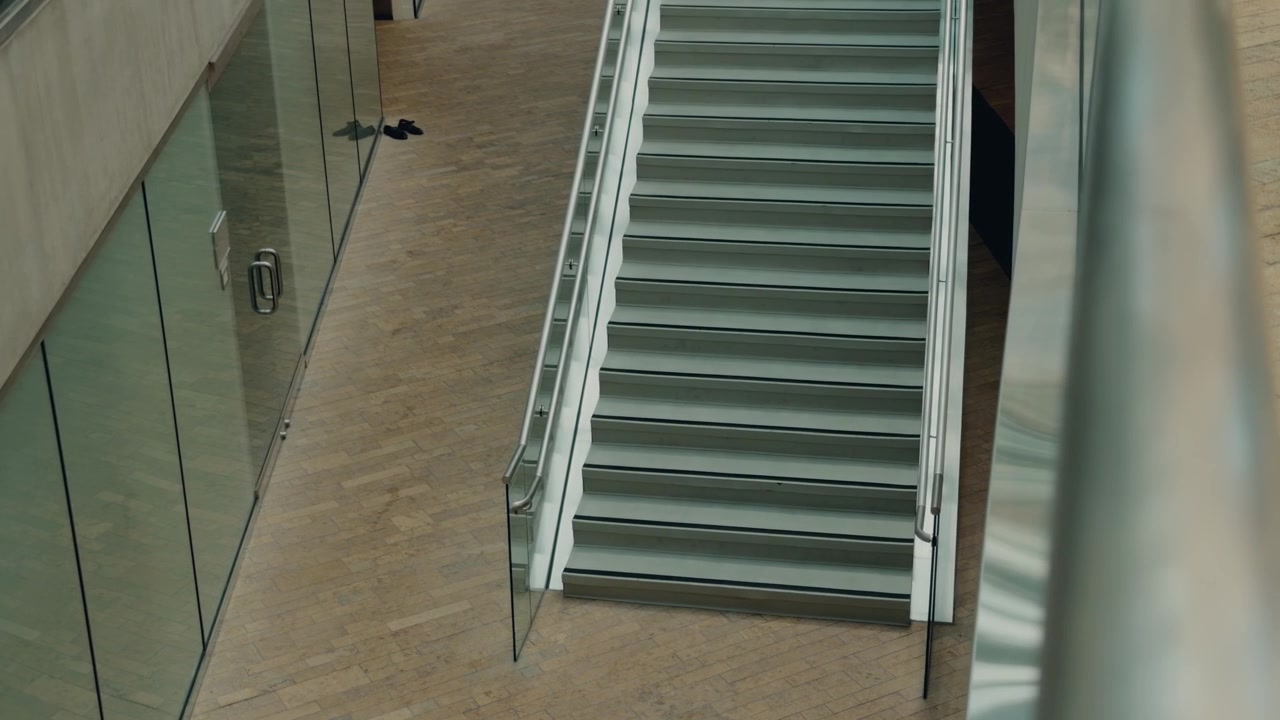 Langsom glidning hen over nederste trapper, mens et glasgelænder passerer i forgrunden.