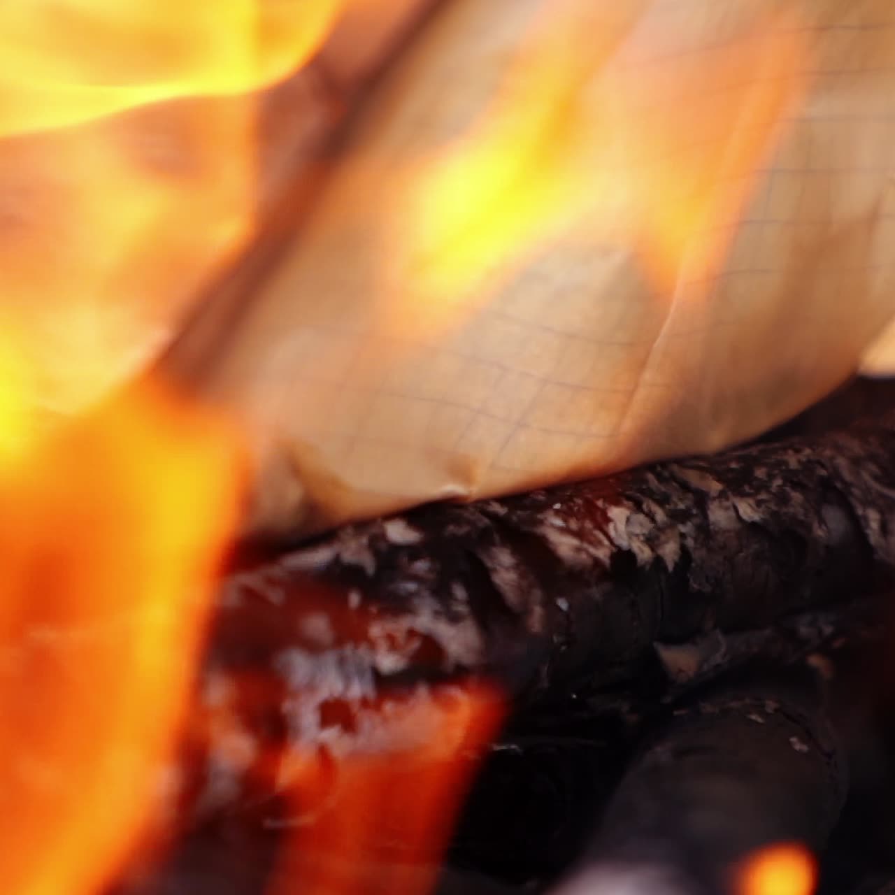 Paper and logs are burning in an outdoor fire. Flames all around. Campsite fire video