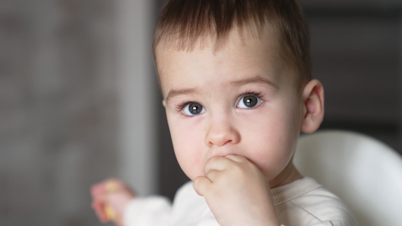 Adorable grey-eyed Caucasian child eating something and smiling sweetly. Close up portrait. Blurred backdrop.