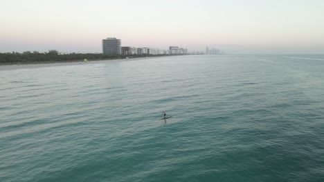 orbiting aerial of stand up ocean paddleboarder alone off miami beach