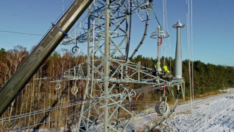 Ascending drone shot of worker in Protection clothes repairing high voltage transmission tower in nature during winter