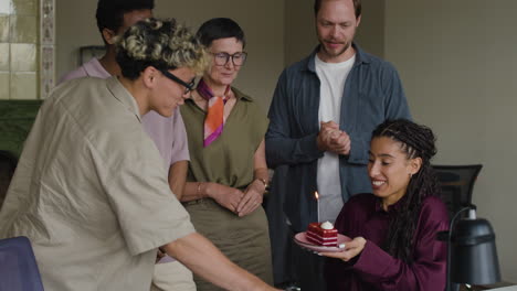 colleagues celebrate a birthday in the office with cake and a candle