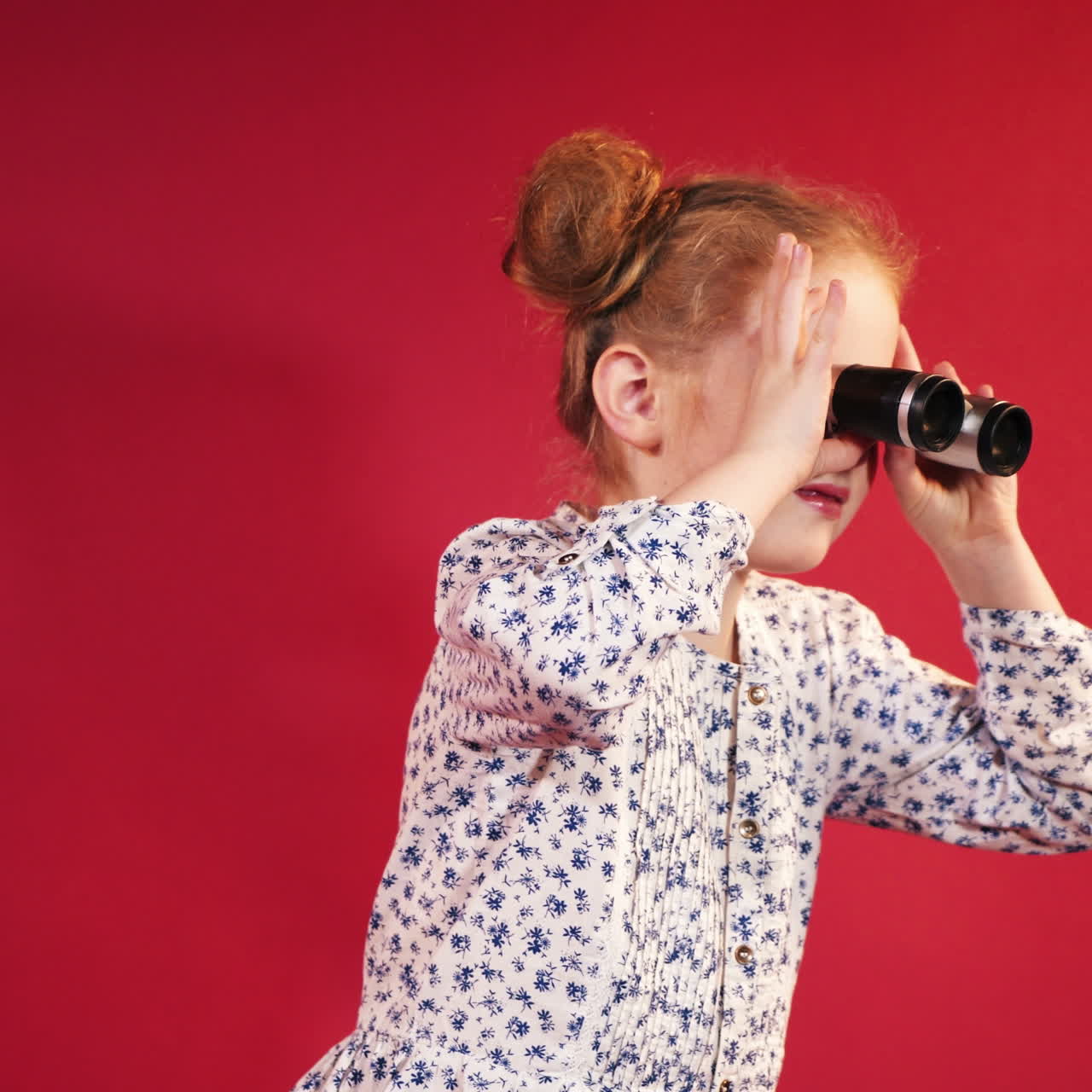 Little girl looking through binoculars. Isolated on red background. Square video