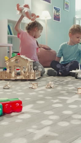 siblings play with baby doll and robot dinosaur in nursery. brother and sister sit on floor enjoying toys view through clearance in construction of cubes