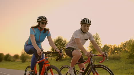 two professional road cyclists ride their bikes on a hill. hand held shot of two strong cyclists female and male on their training on a warm but windy summer day