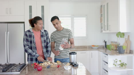 Happy-diverse-gay-male-couple-preparing-healthy-fruit-smoothie-in-kitchen,-copy-space,-slow-motion