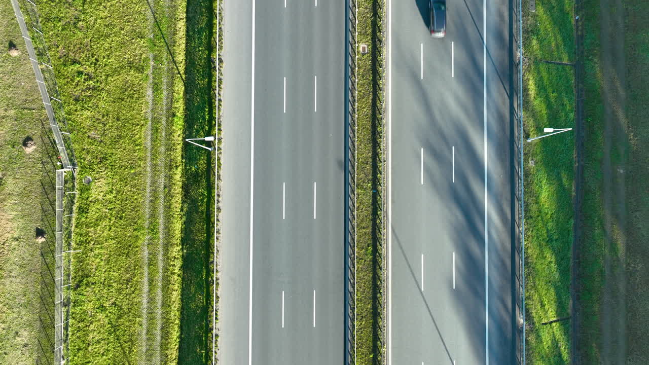 Top‑down drone view of two cars driving on parallel highway lanes with grassy median and clear road markings