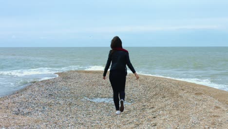 Junge-Frau,-Die-Am-Sandstrand-Vor-Meereswellen-Und-Spritzern-Im-Hintergrund-Spaziert