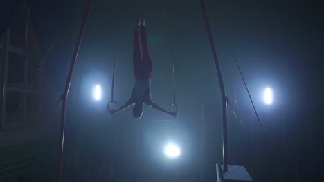 gymnast on a dark background stands on his hands using rings in the air. performs rotation in the olympic program