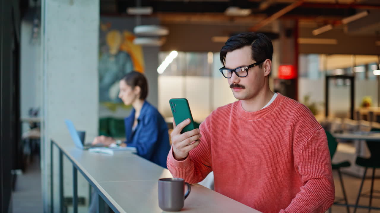 Satisfied guy tapping smartphone in modern coffee shop closeup. Smiling man