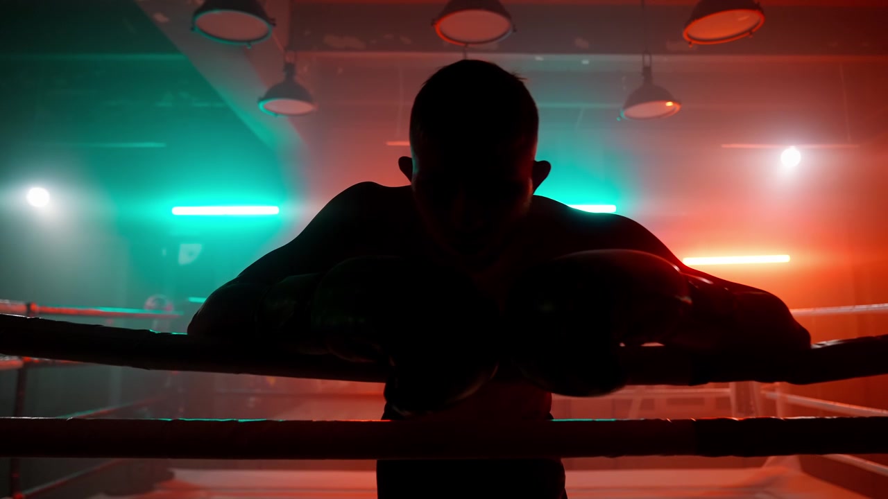Silhouette di un pugile che riposa sulle corde in un ring illuminato al neon.