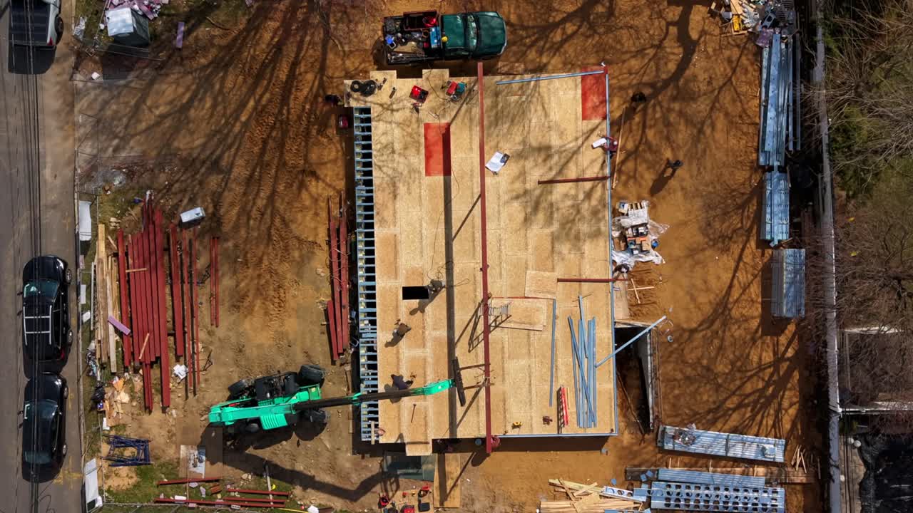 Timelapse aéreo de cima para baixo sobre a construção de uma nova casa em um bairro suburbano de classe média em um dia ensolarado, capturando trabalhadores no local. A câmera inclinou para baixo, aproximando-se do local e dos trabalhadores.