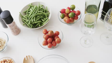 vegetable salad ingredients, condiments, wine and glasses on kitchen work top, slow motion