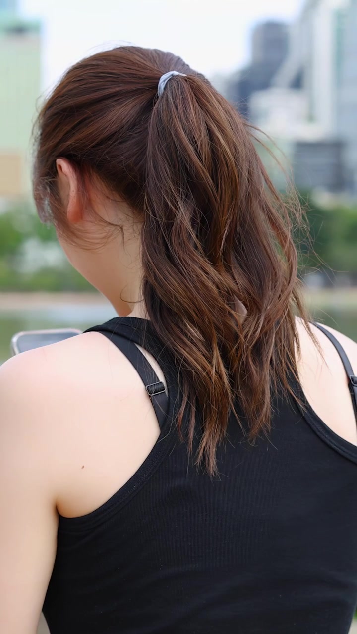 黒いタンクトップを着た女性が屋外でスマートフォンを使用している後ろ姿。