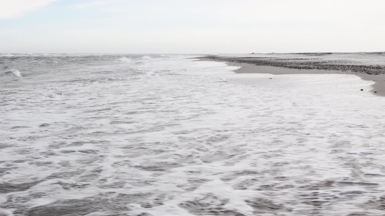 Foamy waves with bubbles reaching empty sandy beach during sunny day. Tilt up shot.