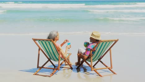 rear view of active senior african american couple toasting drinks on deckchair at beach 4k