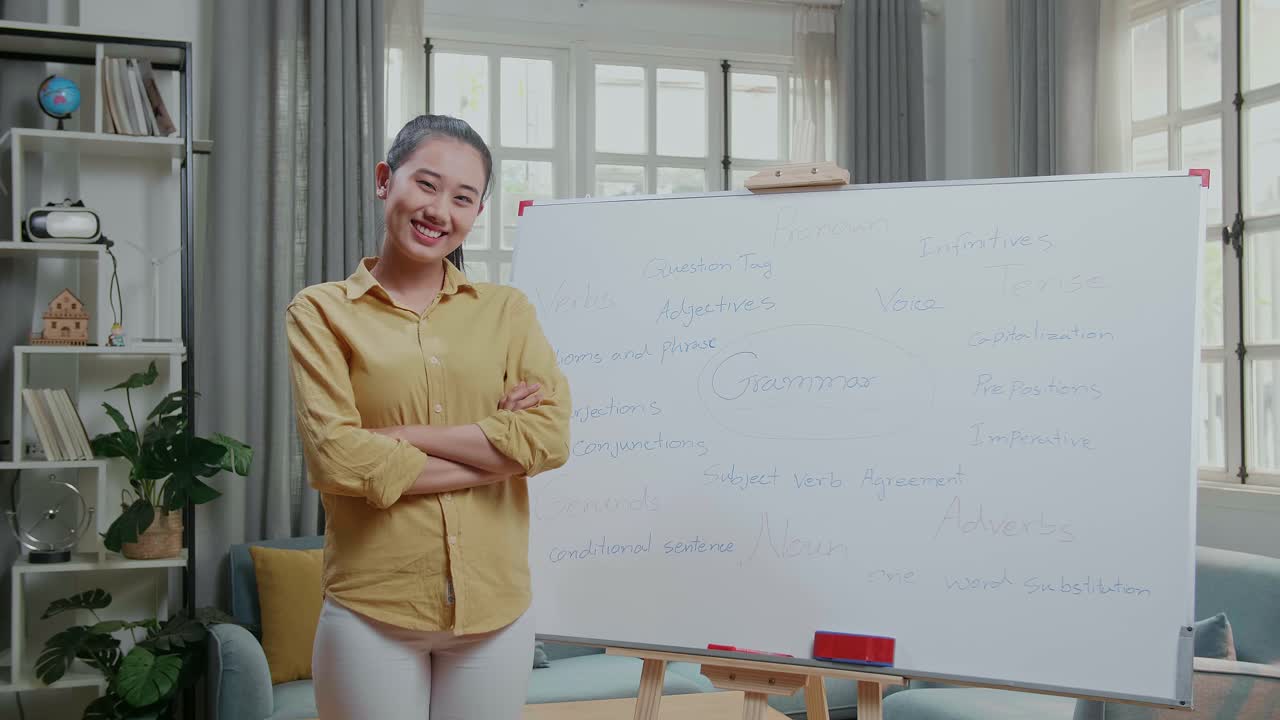 Asian Female Teacher Crossing Arms And Smiling To Camera While Teaching English At Home