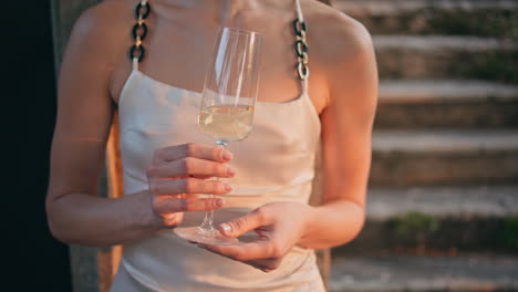 unrecognizable woman holding champagne relaxing under evening sunlight outdoors.