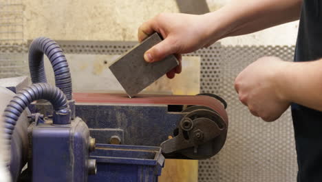 Factory-Worker-Polishing-The-Edges-And-Surface-Of-Metal-Block-With-Linishing-Machine---close-up-shot