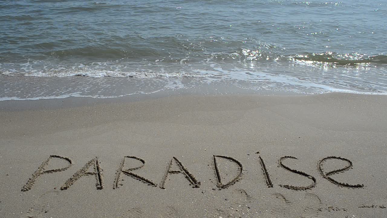 Indskrift "Paradis" i sandet på en tropisk ø. Optagelse på stranden