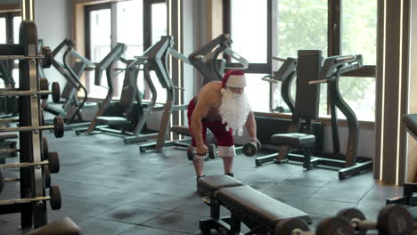 Papá-Noel-Haciendo-Columpios-Con-Mancuernas-En-El-Gimnasio.-Hombre-Disfrazado-De-Santa-En-El-Club-Deportivo