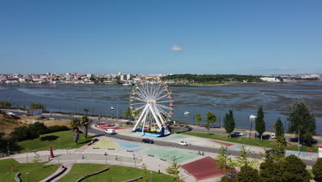 Coches-Circulando-Por-La-Carretera-Alrededor-De-La-Rueda-De-La-Fortuna-En-El-Parque-De-La-Ciudad-Con-Vistas-Al-Río-En-Seixal,-Portugal