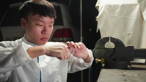 chinese technician in white lab coat picks up protective glasses, puts them on, and picks up tablet in automotive repair workshop with parked white car in background