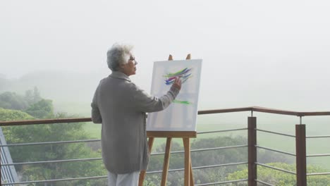 african american senior woman painting on canvas in the balcony at home