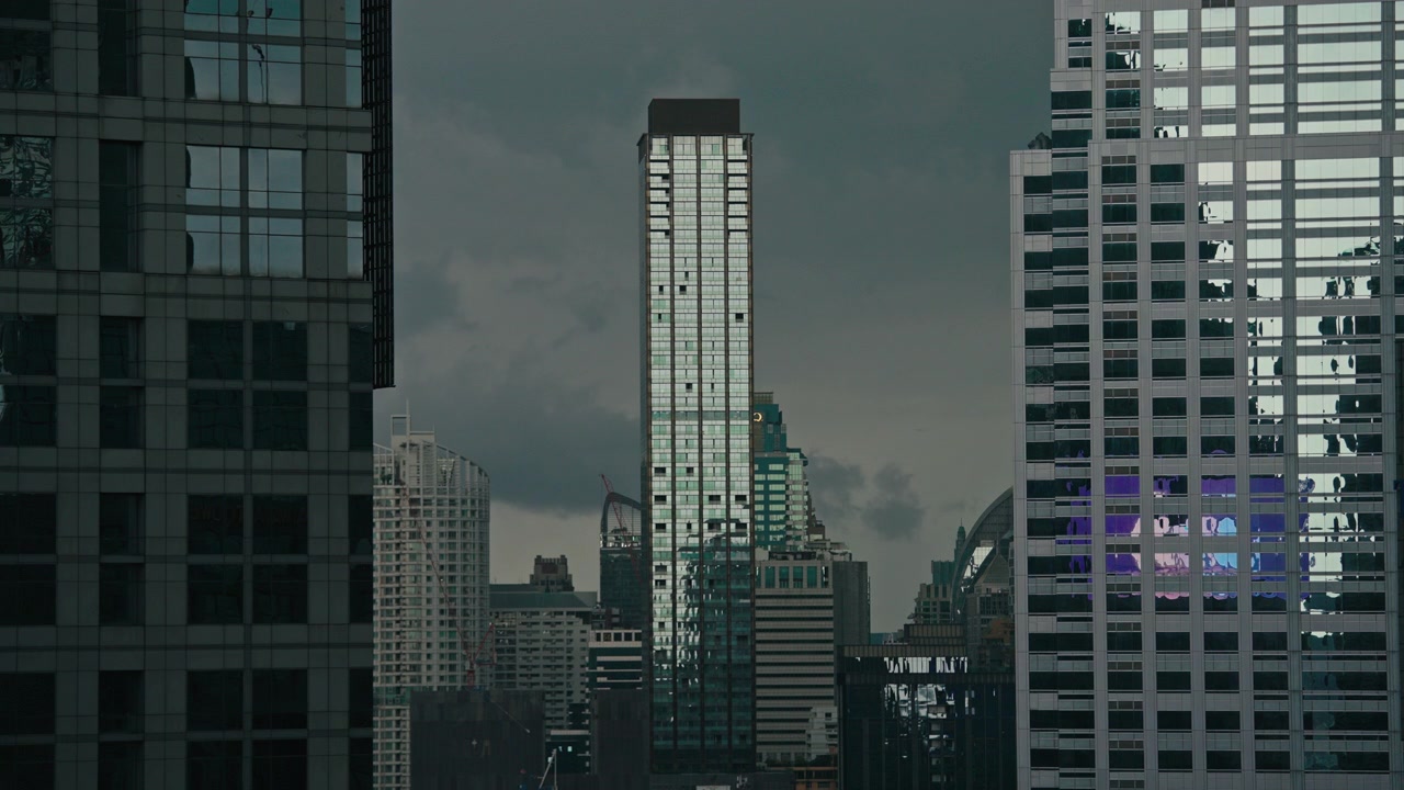 Altos edificios de cristal se alzan contra un cielo tormentoso, reflejando el paisaje urbano. Adecuado para temas de paisajes urbanos o contenido relacionado con el clima. Toma larga estática 4K.