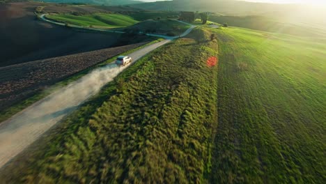 aerial view of a car driving through dirt road along the green grassland at sunset