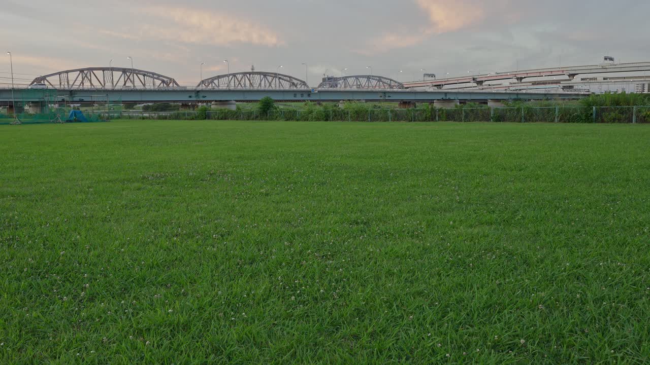 A wide, low-angle shot of a lush green field with the Horikiri Bridge in the background