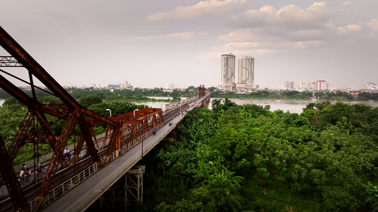 Closeup of Long Bien bridge iron beams structure with mopeds traffic and Hanoi city skylines in background, Drone shot