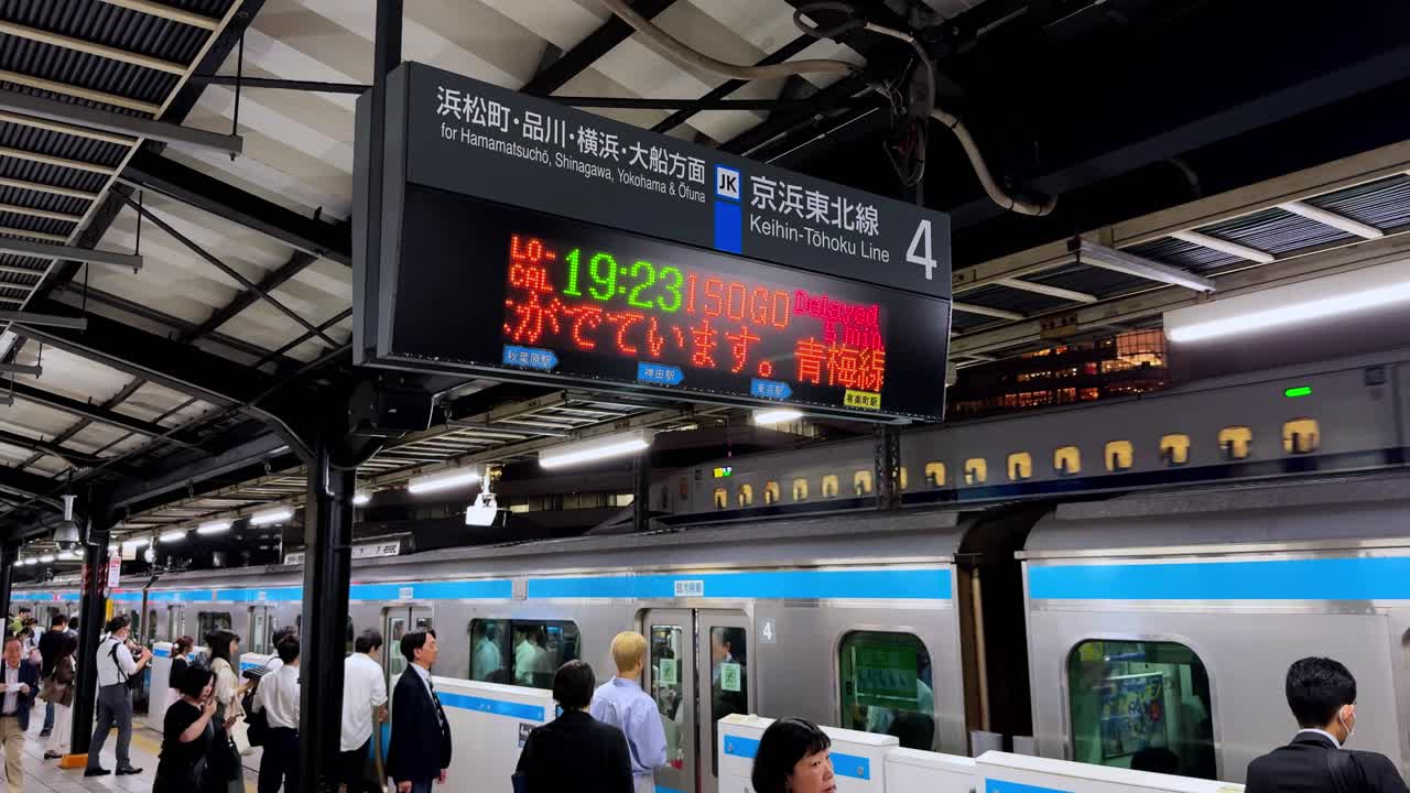 Evening at a busy Tokyo train station with electronic signs and commuters waiting for trains