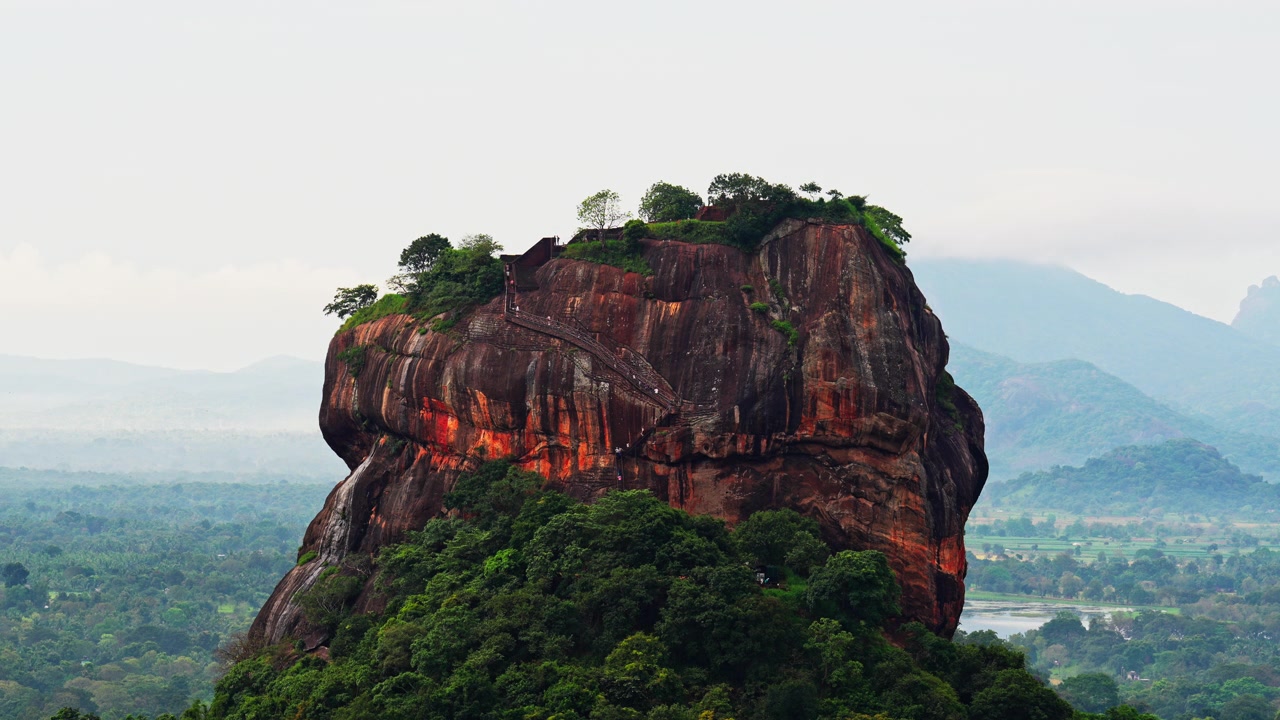 La luz matutina ilumina los escarpados acantilados de la fortaleza de roca de Sigiriya, con su cima cubierta de vegetación y sus famosas escaleras aferradas a la cara de piedra