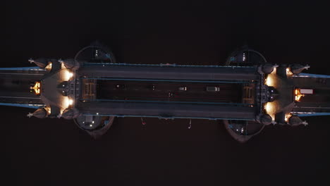 Aerial-birds-eye-overhead-top-down-panning-view-of-illuminated-Tower-Bridge-across-River-Thames-in-evening.-Cars-driving-over-bridge.-London,-UK