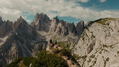 Parralax-drone-shot-with-tourists-watching-panoramic-view-with-tall-steep-rocky-mountains,-partly-clouded-sky-in-the-background,-hiking-in-the-Alps,-majestic-landscape,-cinematic-color-grade