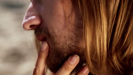 the woman gently strokes the man's beard as they sit together on the beach - close up