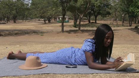 una niña africana en el parque leyendo tranquilamente un libro, tiro estático