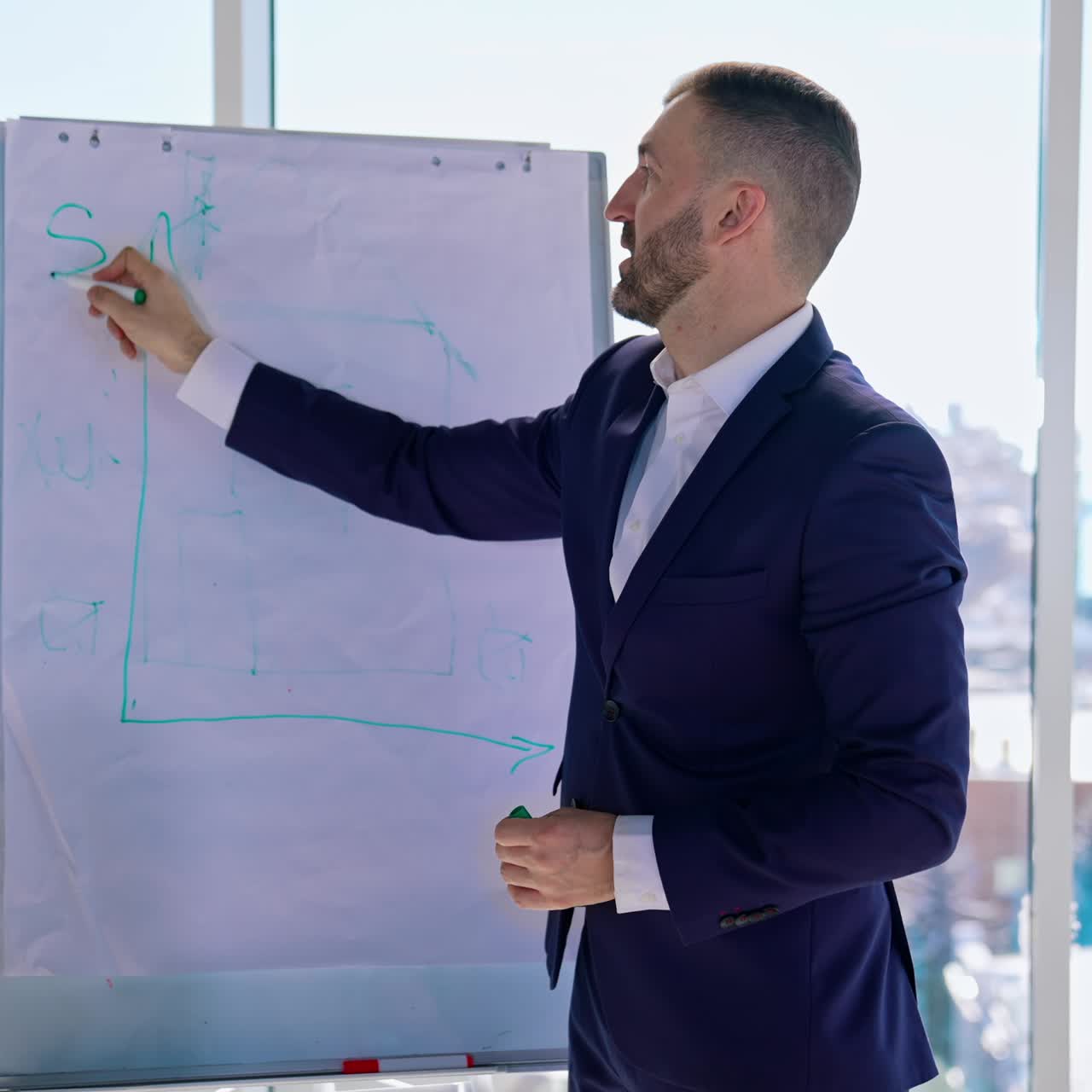 Manager che disegna su una lavagna bianca in un ufficio luminoso. Affascinante uomo d'affari in abito che mostra la sua nuova strategia con lo sfondo della città dalla finestra. Concetto aziendale.