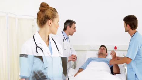 Médicos-Hablando-Con-Un-Paciente-Enfermo-En-La-Cama-Mientras-Uno-Revisa-La-Radiografía
