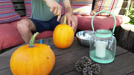 young dad carves pumpkin on garden terrace, sunny autumn day