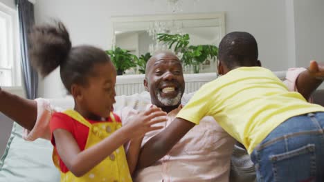 Happy-african-american-grandfather-and-grandchildren-hugging-on-sofa