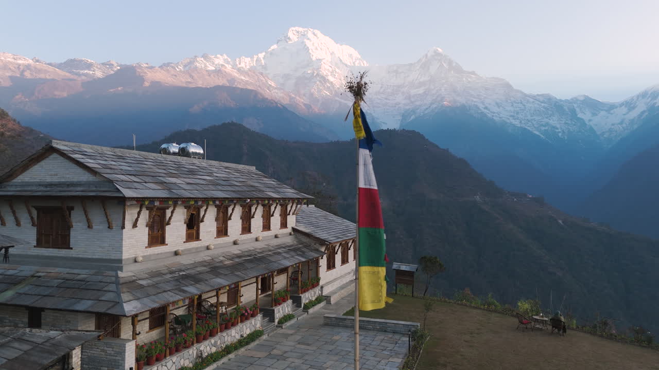 Aerial drone view of a traditional home in Ghandruk Village, Kaski, Nepal, with Annapurna and Machhapuchhre mountain ranges in the background. Showcases Nepal's tourism appeal