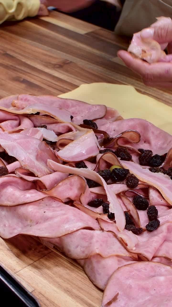 Mani che preparano pane al prosciutto con cura e attenzione su un tavolo di legno.