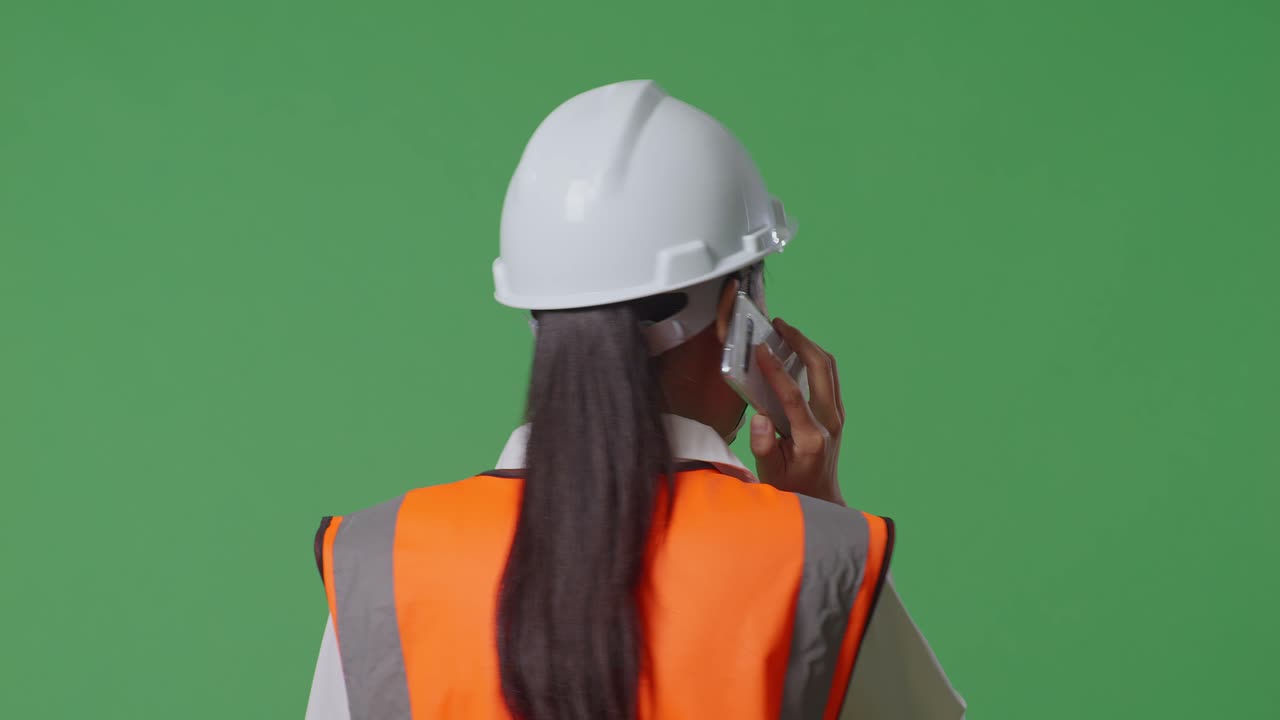 안전 헬을 착용한 아시아 여성 엔지니어가 녹색 화면 배경 스튜디오에서 는 동안 스마트폰으로 대화하는 근접 뒷면