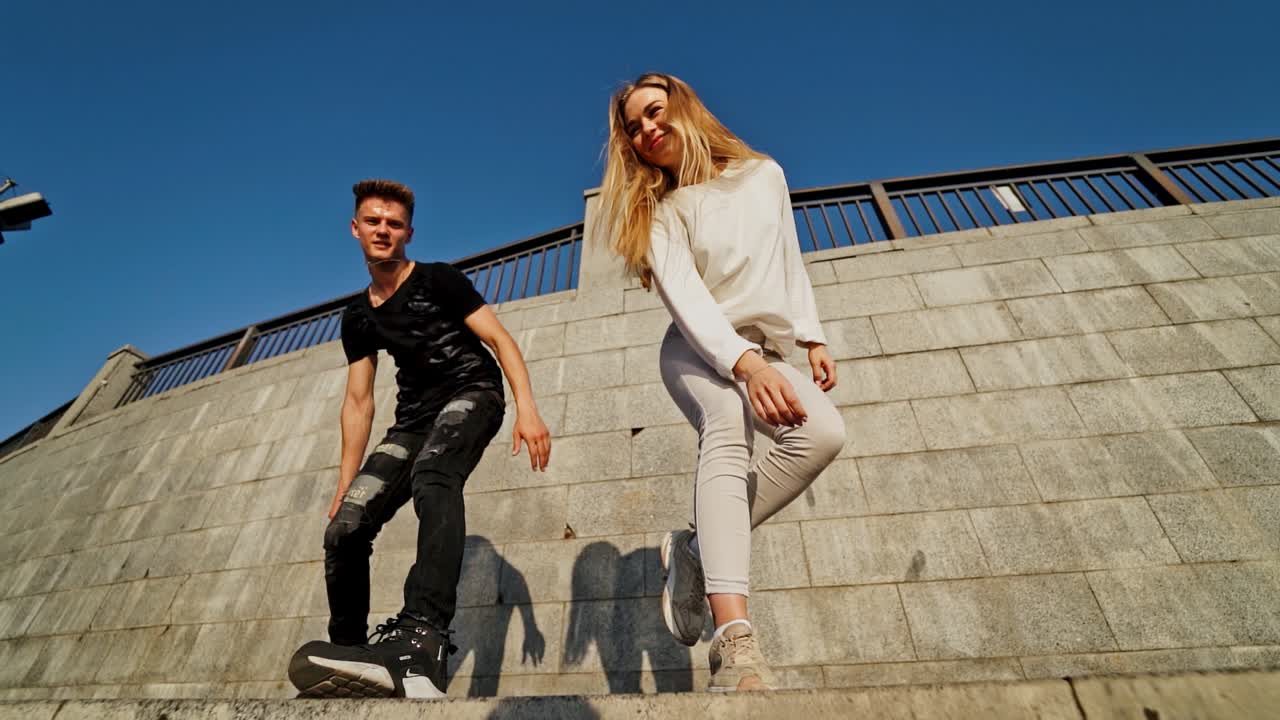 Modern dancers in the street. Urban lifestyle. Hip-hop generation. Boy's and girl's emotional moves on the video. Young couple at stone wall background is looking into the camera.
