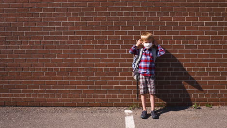 little boy standing in a school yard puts on his mask