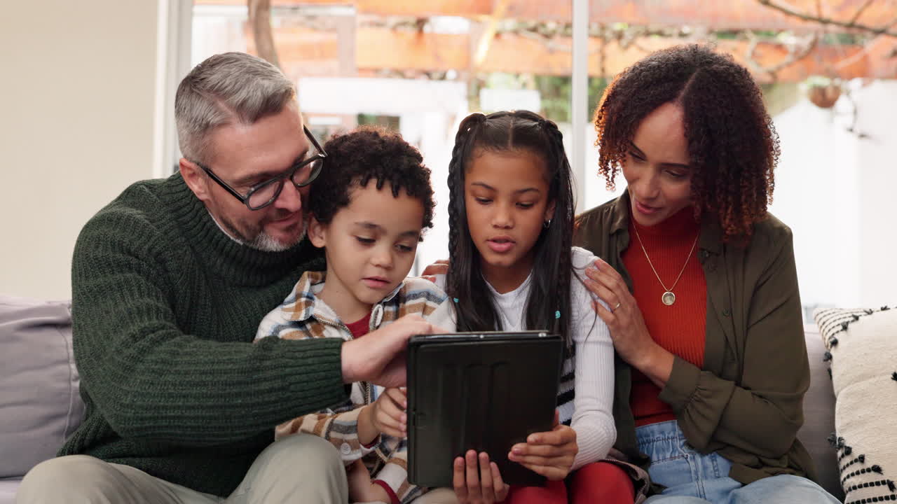 Happy Family of Four Looking at Tablet Together on Sofa